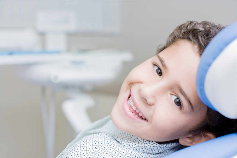 Brunette boy smiles while sitting in the treatment chair at his pediatric dentist in Austin, TX