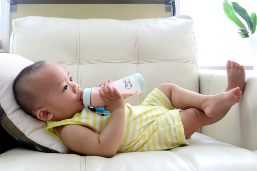 Baby lies on the couch sucking on a bottle, increasing their risk of baby bottle tooth decay