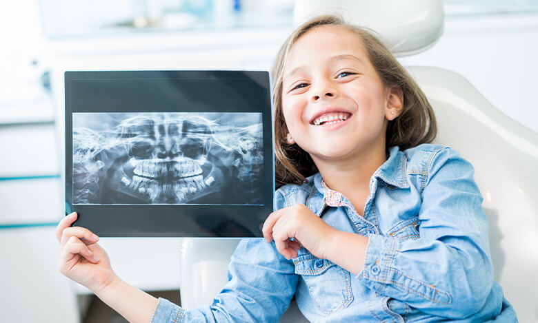 smiling girl holding up an x-ray of her mouth