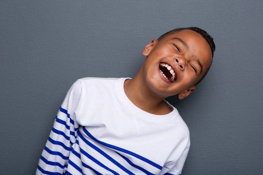 Boy in a white and blue striped shirt smiles after receiving a dental crown on one of his baby teeth