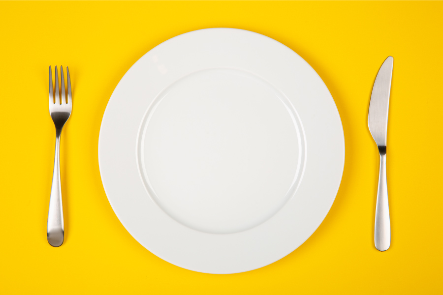 Aerial view of a white plate and silverware on a yellow table in the fall