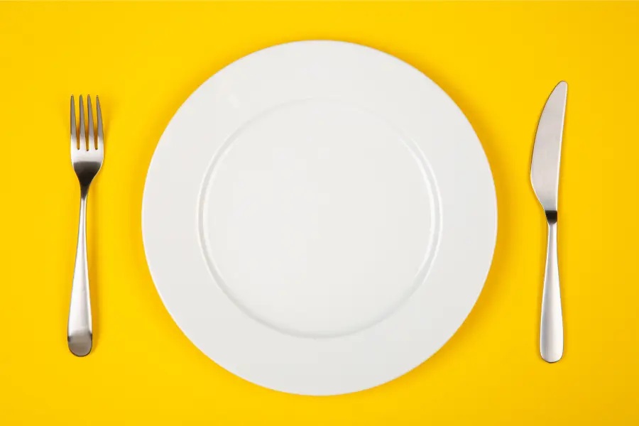Aerial view of a white plate and silverware on a yellow table in the fall