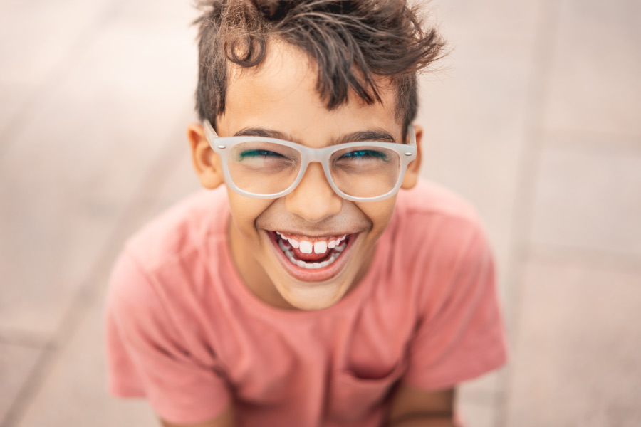 Brunette boy wearing glasses smiles while wearing a salmon-colored shirt