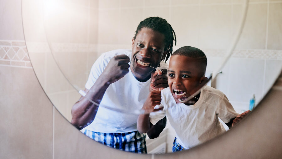 Dad and son floss their teeth together while looking in the bathroom mirror in Austin, TX