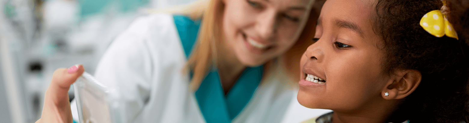 dentist using a mirror to show a young girl her teeth